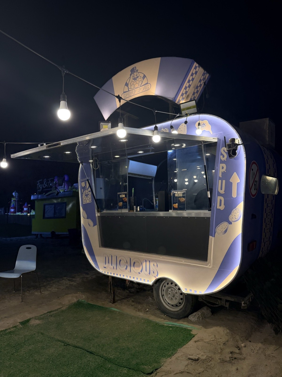 Side view of the illuminated Spudlicious food truck at night in Busaiteen